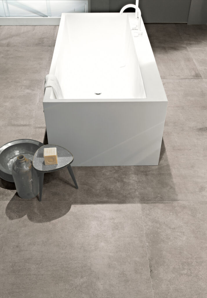 Salle de bain avec baignoire blanche, tabouret bas avec cube de savon et sol en grès cérame gris chaud