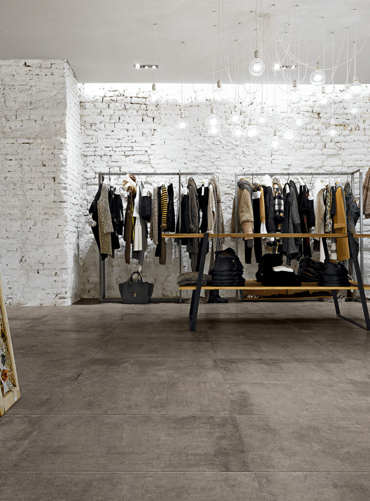 Magasin de vêtements avec portants et établi, mur en pierre blanche et sol en grès cérame.