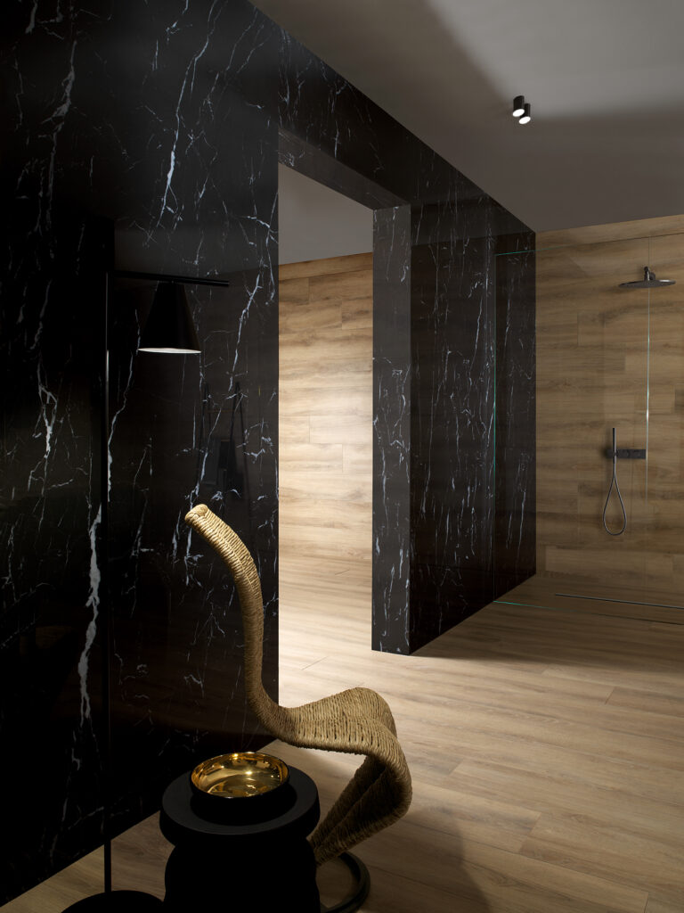 Badezimmerwand verkleidet mit schwarzem Feinsteinzeug in Marmoroptik mit heller Äderung.
