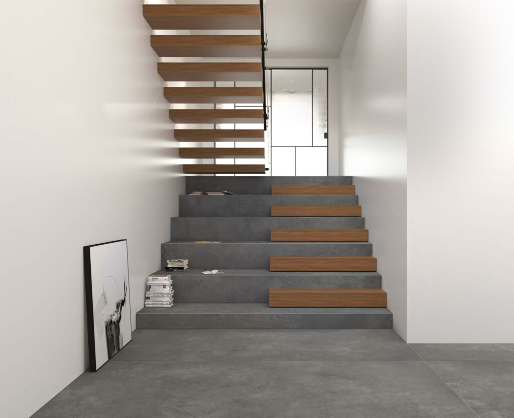 Escalier intérieur d’un appartement, habillé de grès cérame effet béton gris foncé.