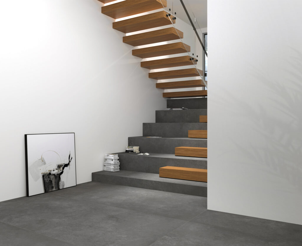 Escalier intérieur d’un appartement, habillé en grès cérame effet béton gris foncé.