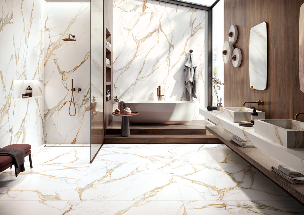 Bagno decorato con la collezione Calacatta Gold: piastrelle in gres porcellanato dal fondo bianco paglierino, intervallata da venature giallo-oro. Le piastrelle sono state applicate a pavimento, rivestimento e come arredi di interior design come i lavabi