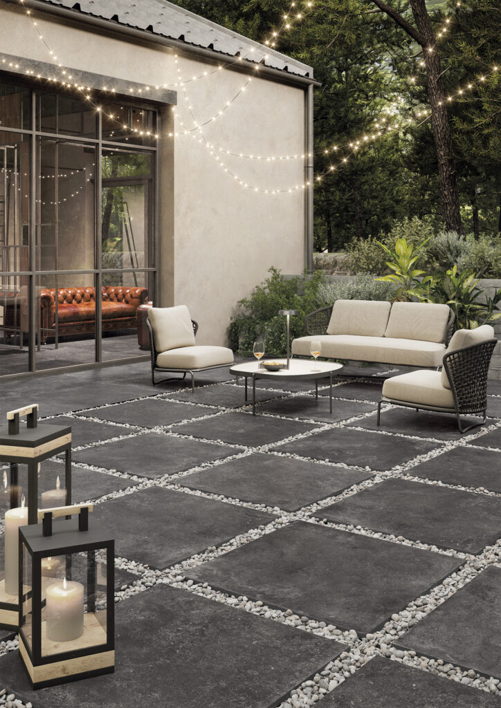 Espace de vie extérieur avec canapés et chaises, dalles en grès cérame effet pierre foncée, pose sur gravier