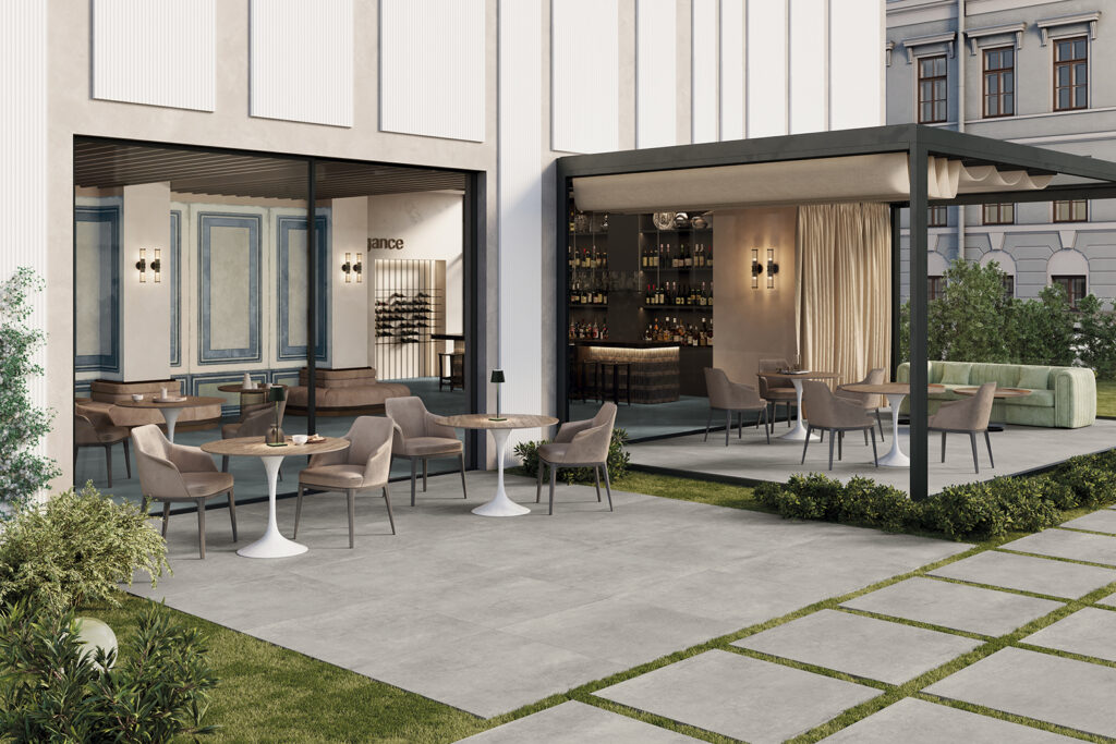 giardino di un bar con tavolini e veranda rivestita in gres effetto cemento grigio chiaro